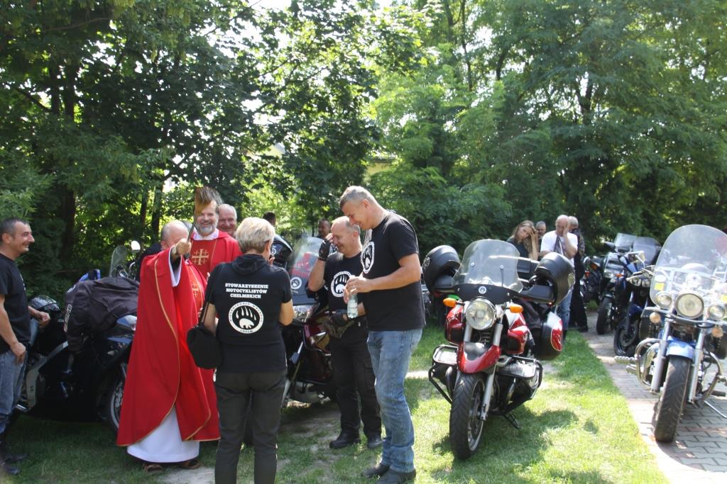 Ksiądz w czerwonej sutannie dokonuje poświęcenia motocykli stojących na dworze