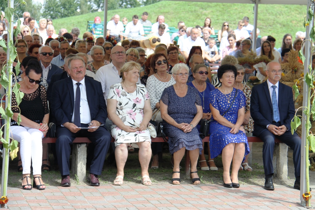 Uczestnicy dożynek siedzą na krzesłach w tym zaproszeni goście