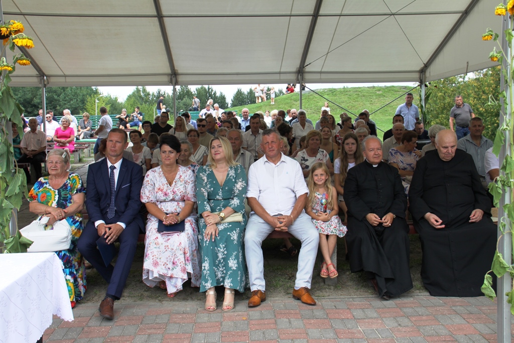 Uczestnicy dożynek siedzą pod zadaszeniem - wśród gości między innymi księża